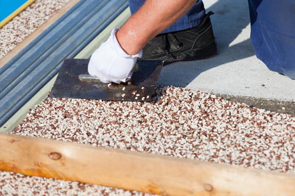 This image shows a man putting pebbles on concrete that is being resurfaced.